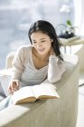 Cinese donna lettura libro sul divano in casa interiore — Foto stock