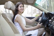 Chinese woman driving car and looking in camera — Stock Photo