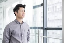 Hombre de negocios chino mirando hacia otro lado y sonriendo en la oficina - foto de stock