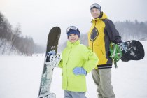 Chino padre e hijo de pie con tablas de snowboard en pendiente - foto de stock