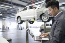 Chinesischer Automechaniker mit Laptop in der Werkstatt — Stockfoto