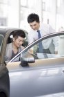 Chinese car dealer helping client choosing car in showroom — Stock Photo
