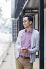 Китаец, стоящий на улице и держащий смартфон — стоковое фото