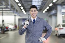 Chinese auto mechanic standing in workshop with tool — Stock Photo