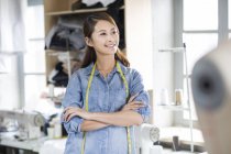 Chinese female fashion designer standing with arms folded in atelier — Stock Photo