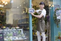 Chinese florist holding open sign in store doorway — Stock Photo