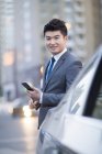 Uomo d'affari cinese in piedi in auto con smartphone — Foto stock