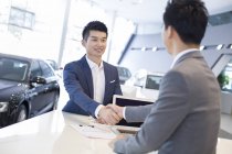 Chinese man shaking hands with car dealer in showroom — Stock Photo