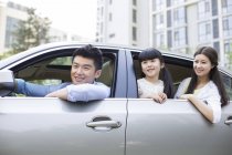 Familia china que monta y se inclina fuera del coche - foto de stock