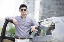 Chinese man in sunglasses standing at car open door — Stock Photo