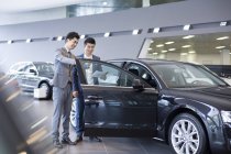Китайський автомобілів дилер допомагаючи клієнт виборі автомобіль в автосалоні — стокове фото