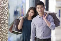Китайская пара стоит с сумками в торговом центре — стоковое фото