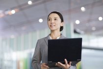 Chinesische Geschäftsfrau steht mit Laptop drinnen — Stockfoto