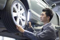 Mecánico auto chino examinando coche con linterna - foto de stock