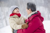 Chinese grandfather and grandson embracing on snow — Stock Photo