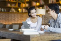 Chino joven y mujer hablando con tazas de café en la cafetería - foto de stock