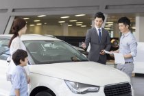 Vendeur de voitures chinois aider la famille à choisir la voiture dans le showroom — Photo de stock