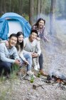 Amici cinesi seduti accanto al falò nella foresta — Foto stock
