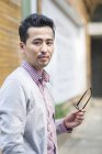 Chinese man holding pair of glasses and looking in camera — Stock Photo