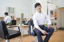 Cabeleireiro chinês sentado na cadeira na barbearia — Fotografia de Stock