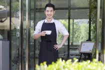 Ladenbesitzer steht mit Tasse Kaffee vor Tür des Cafés — Stockfoto