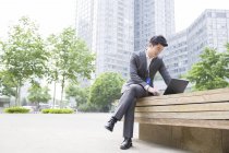 Chinese businessman working with laptop on street bench — Stock Photo