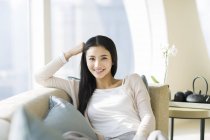 Chinesische Frau lehnt sich auf Sofa und schaut in die Kamera — Stockfoto