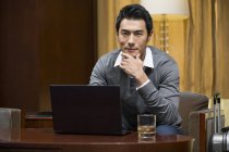 Uomo d'affari cinese che utilizza il computer portatile a tavola in camera d'albergo — Foto stock