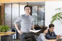 Chinese male IT worker standing with papers in office — Stock Photo