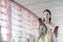 Chinese woman holding smartphone and ticket at airport — Stock Photo