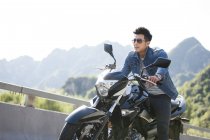 Hombre chino sentado en motocicleta en la carretera - foto de stock