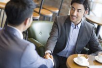 Chinese businessmen shaking hands in cafe — Stock Photo
