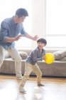 Китайський батько і син, граючи з жовту кулю у вітальні — стокове фото