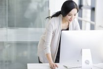 Mujer china de pie y utilizando la computadora en la oficina - foto de stock
