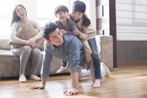 Chinesische Kinder spielen mit Vater auf dem Boden, während Mutter auf dem Sofa lacht — Stockfoto