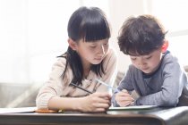 Chinese girl helping brother studying at table — Stock Photo