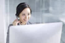 Chinese businesswoman using headset at workplace — Stock Photo