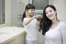 Chinese girl combing mother hair in bathroom — Stock Photo