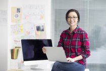 Chinese woman sitting on office desk with laptop — Stock Photo