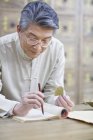 Senior Chinese doctor holding medicinal herb and writing in notebook — Stock Photo