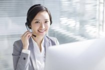 Chinesische Geschäftsfrau benutzt Headset am Arbeitsplatz — Stockfoto