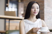 Chinese woman sitting with coffee and looking away — Stock Photo