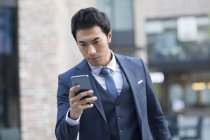 Homme d'affaires chinois utilisant un smartphone dans la rue — Photo de stock