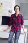 Chinese woman leaning on table in office — Stock Photo