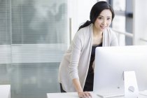 Chinesin steht und benutzt Computer im Büro — Stockfoto