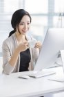 Chinese woman drinking coffee at workplace — Stock Photo