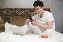 Chinese man using smartphone in bed — Stock Photo