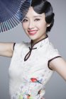 Chinese woman in traditional cheongsam posing with folding fan — Stock Photo