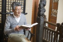 Senior chinesischer Mann sitzt im Stuhl und liest Buch — Stockfoto