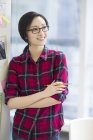 Chinese female designer standing at wall with sketches — Stock Photo